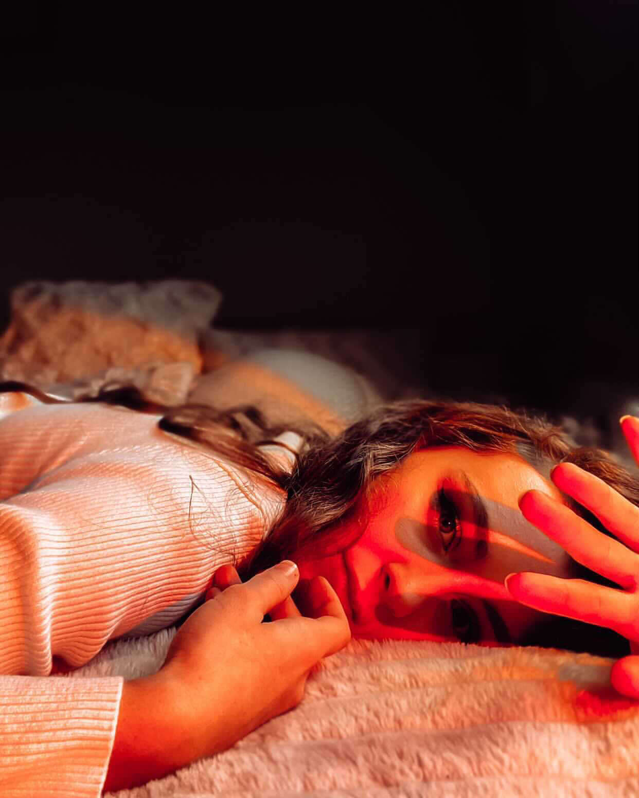 Person resting in bed under the soft orange glow of a sunset lamp, creating a warm and calming bedtime atmosphere.