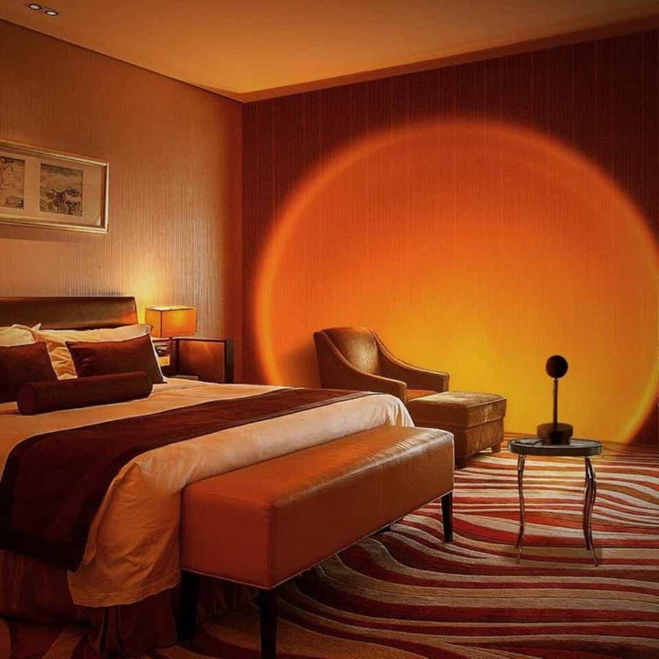 Stylish bedroom lit by a sunset lamp casting a large orange glow on the wall, creating a warm and cozy ambiance with earthy-toned decor.